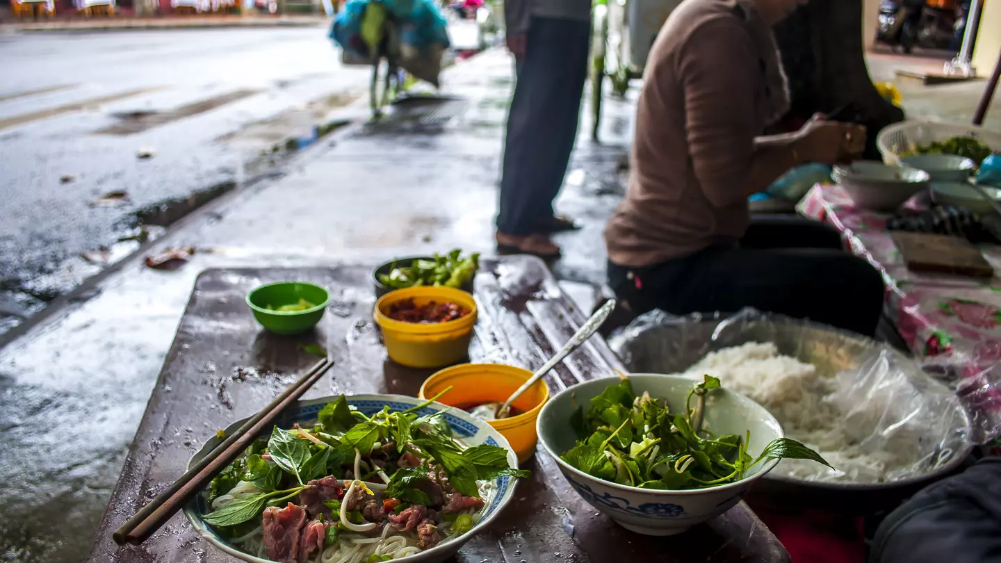 A bowl of pho and a bowl of mint on the street in Vietnam.