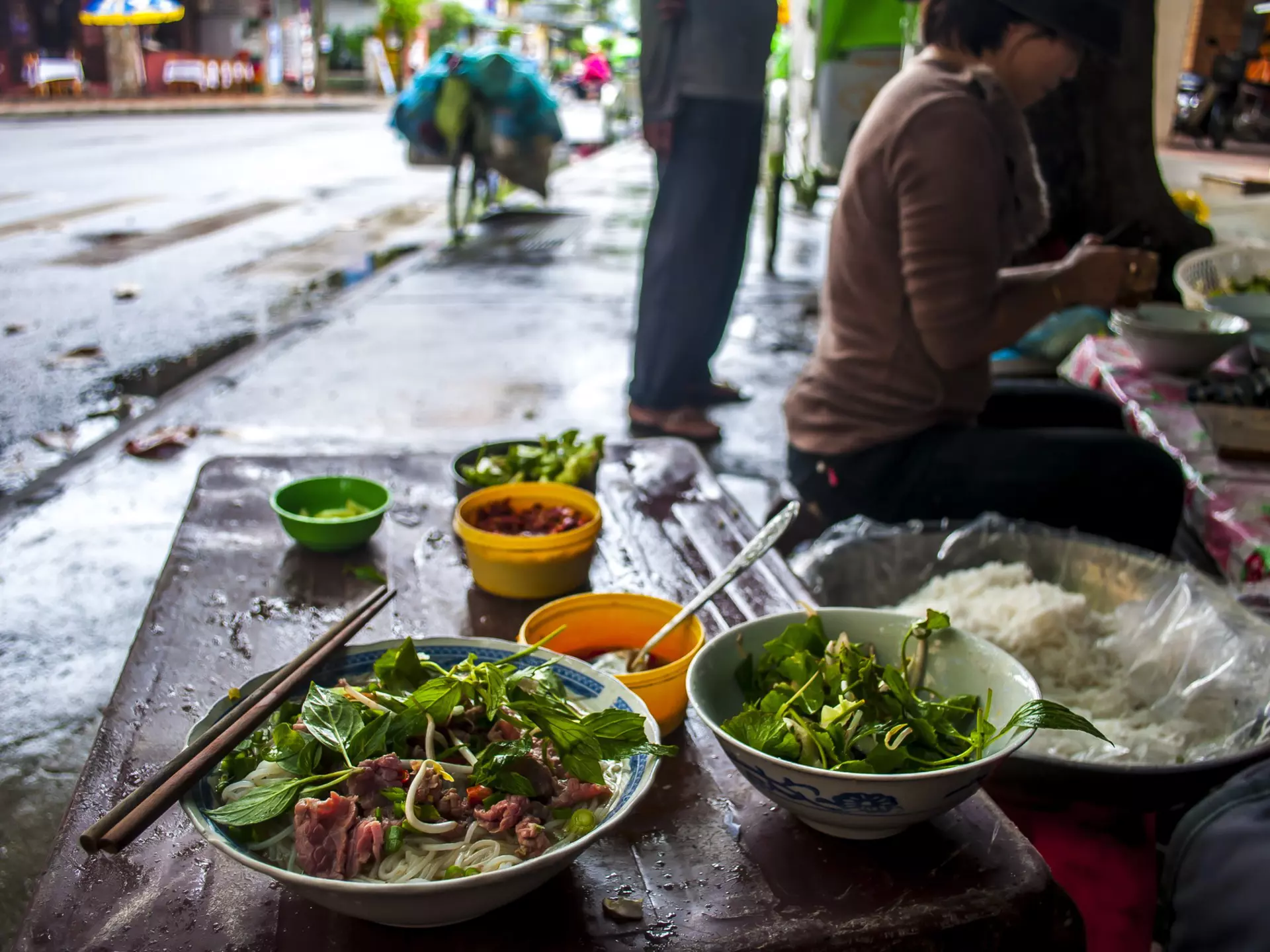 A bowl of pho and a bowl of mint on the street in Vietnam.