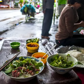 A bowl of pho and a bowl of mint on the street in Vietnam.