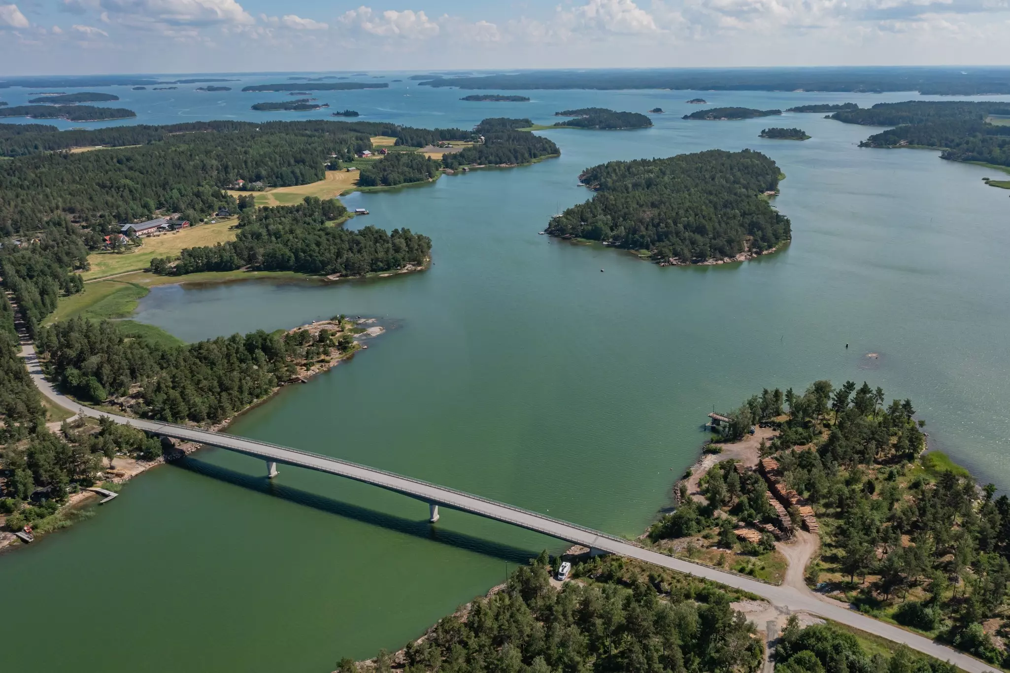 An aerial view of a causeway bridge crossing between two islands covered with green trees. Other islands can be seen in the distance.