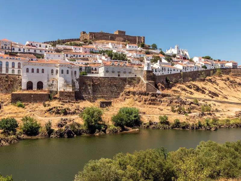 View of a whitewashed village and a medieval castle overlooking a river on a sunny day