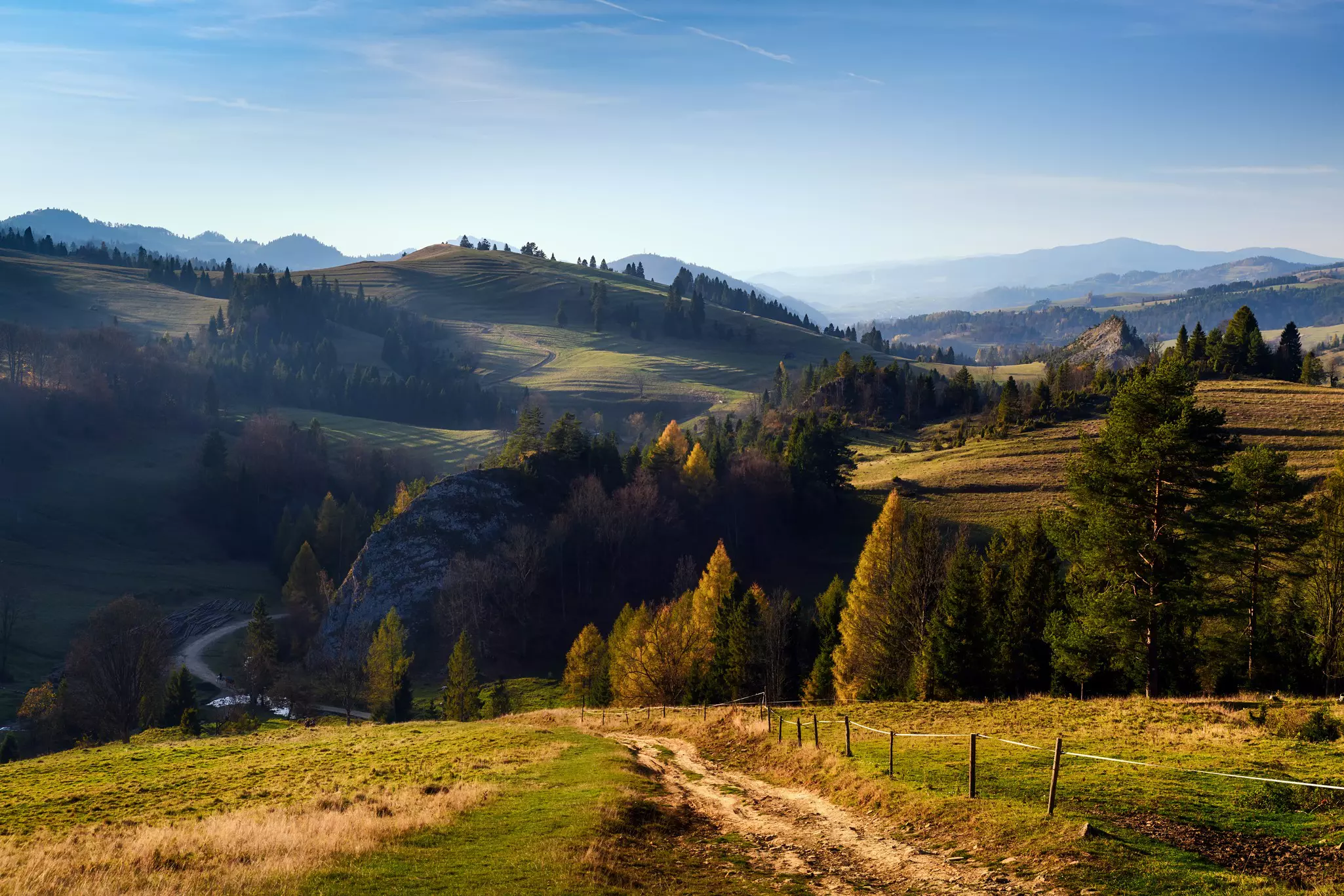 Autumn panorama of mountains in the distance with a dirt path leading toward them on a mostly sunny day.