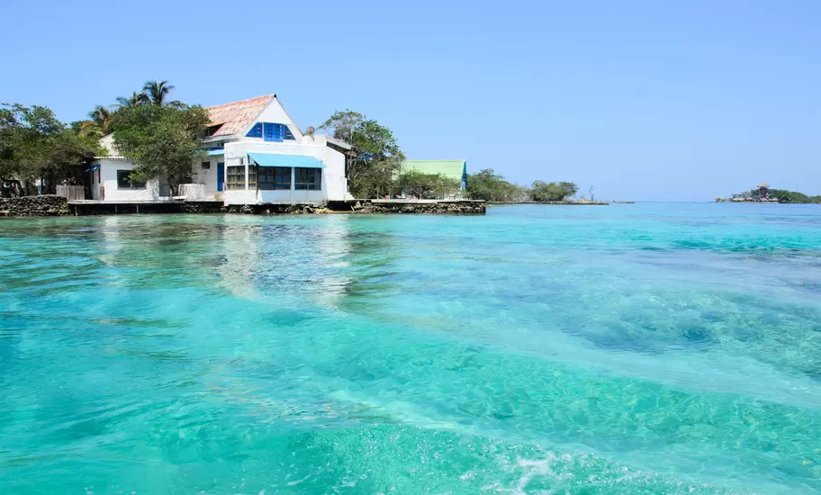 White island house with blue shutters on a rocky islet in the Islas del Rosario, Colombia, above turquoise water