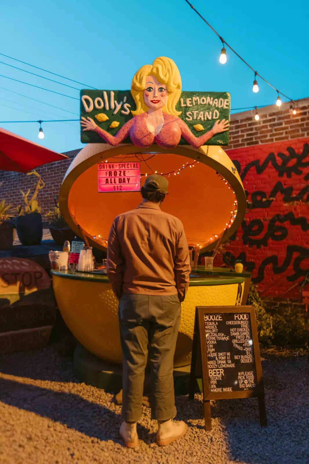 A man waits in front of a lemon-shaped bar labeled "Dolly's lemonade stand" 