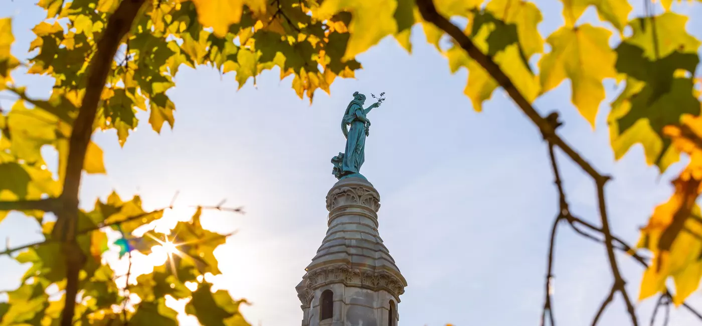 amber foliage frames a green statue of a woman atop a column