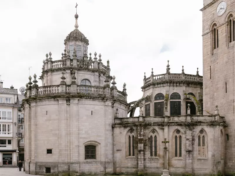 Woman in a trench coat walking through an empty square in Lugo