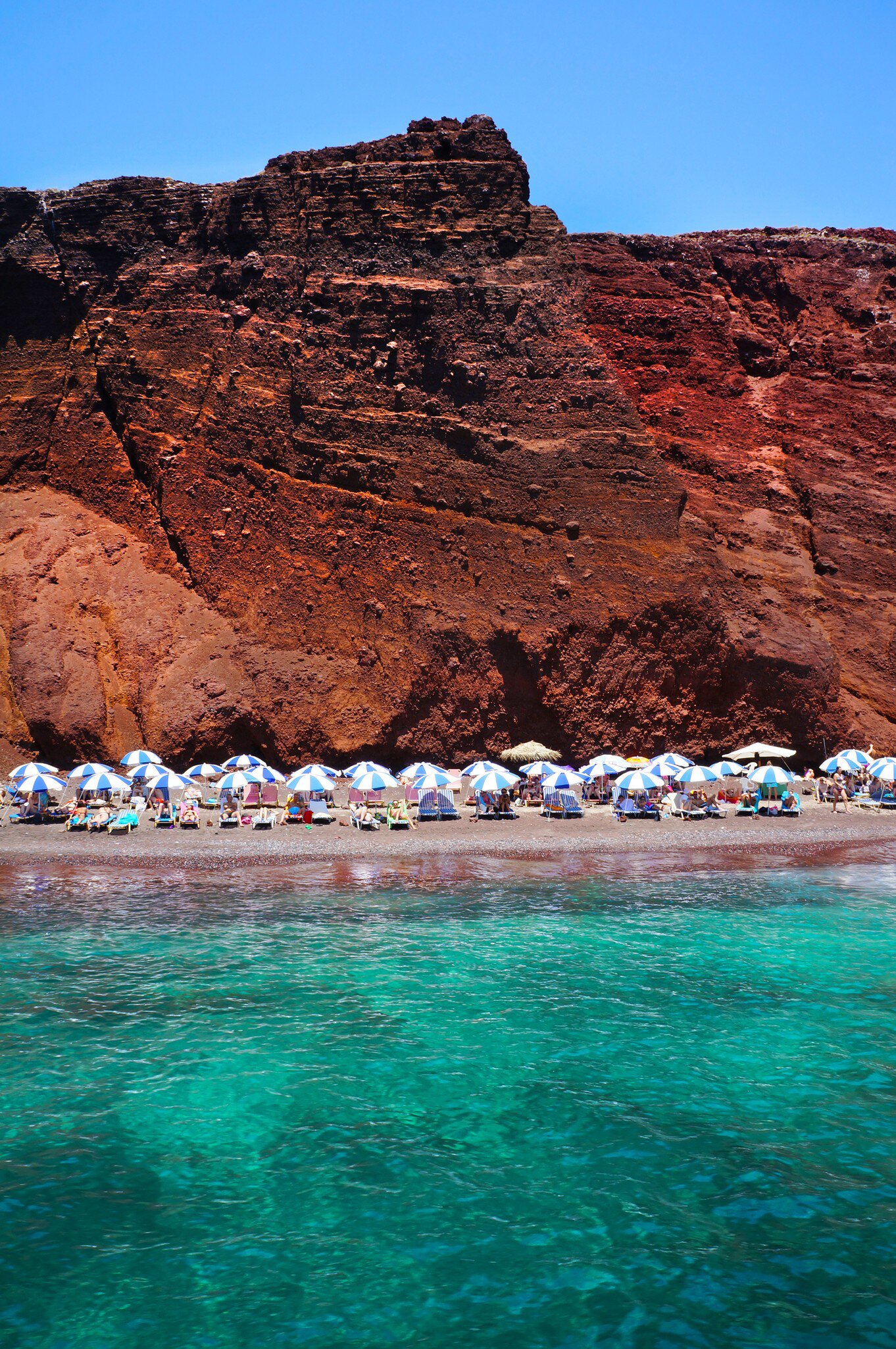 Tourists lounge on beach chairs on Red (Kokkini) Beach on Santorini island, Greece