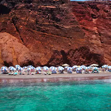 Tourists lounge on beach chairs on Red (Kokkini) Beach on Santorini island, Greece