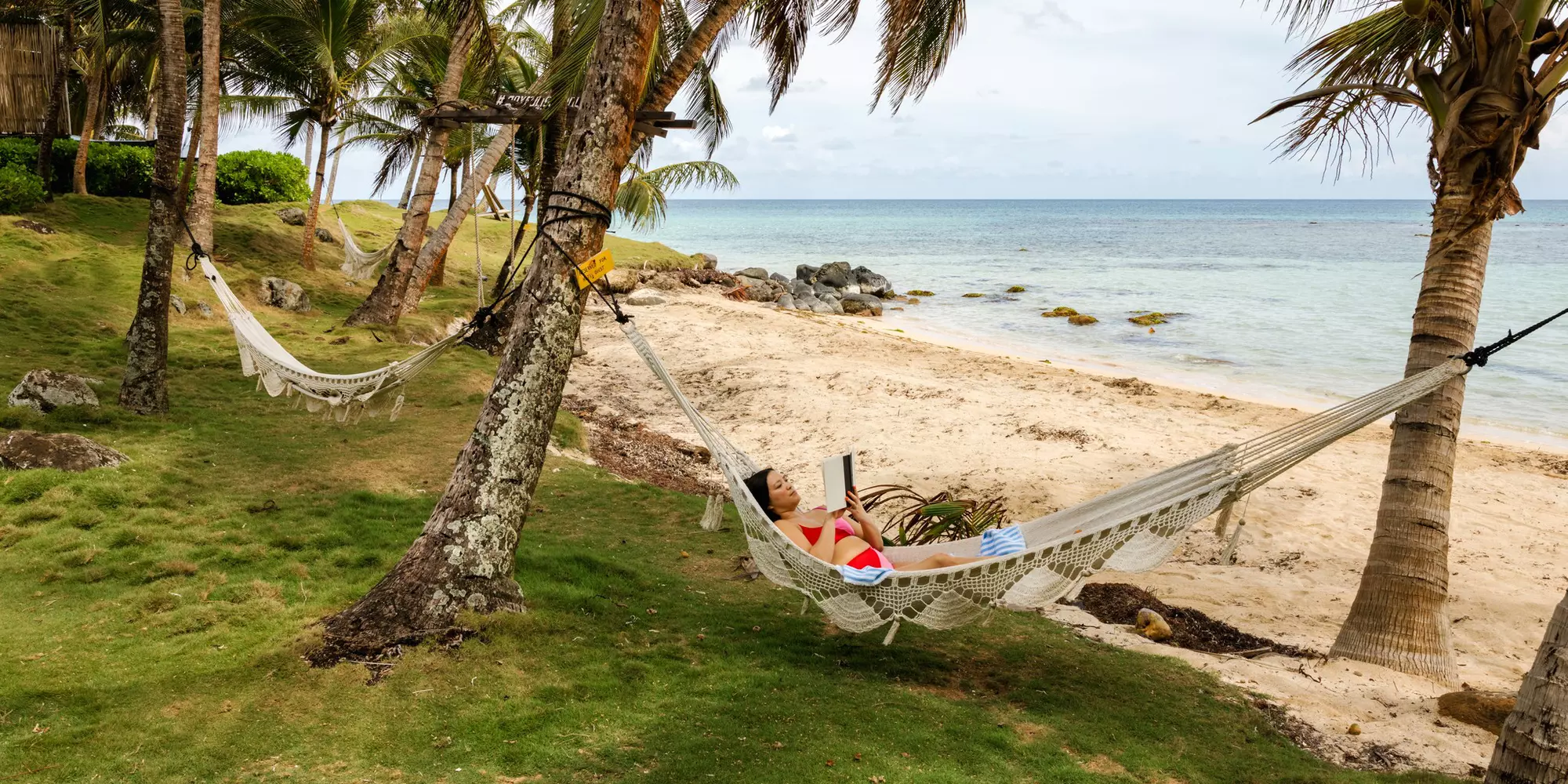 Woman relaxing in a hammock on the beach and reading. Little Corn Island, Nicaragua. May 2025.