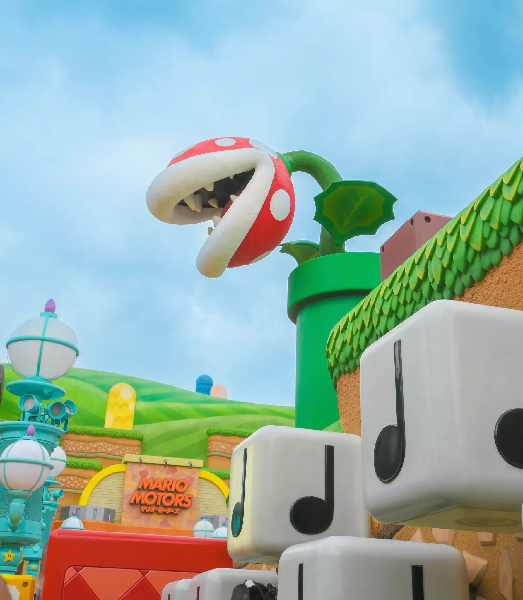 A large plant-like sculpture with a teeth-filled mouth leans over a colorful exterior of a ride at a theme park.