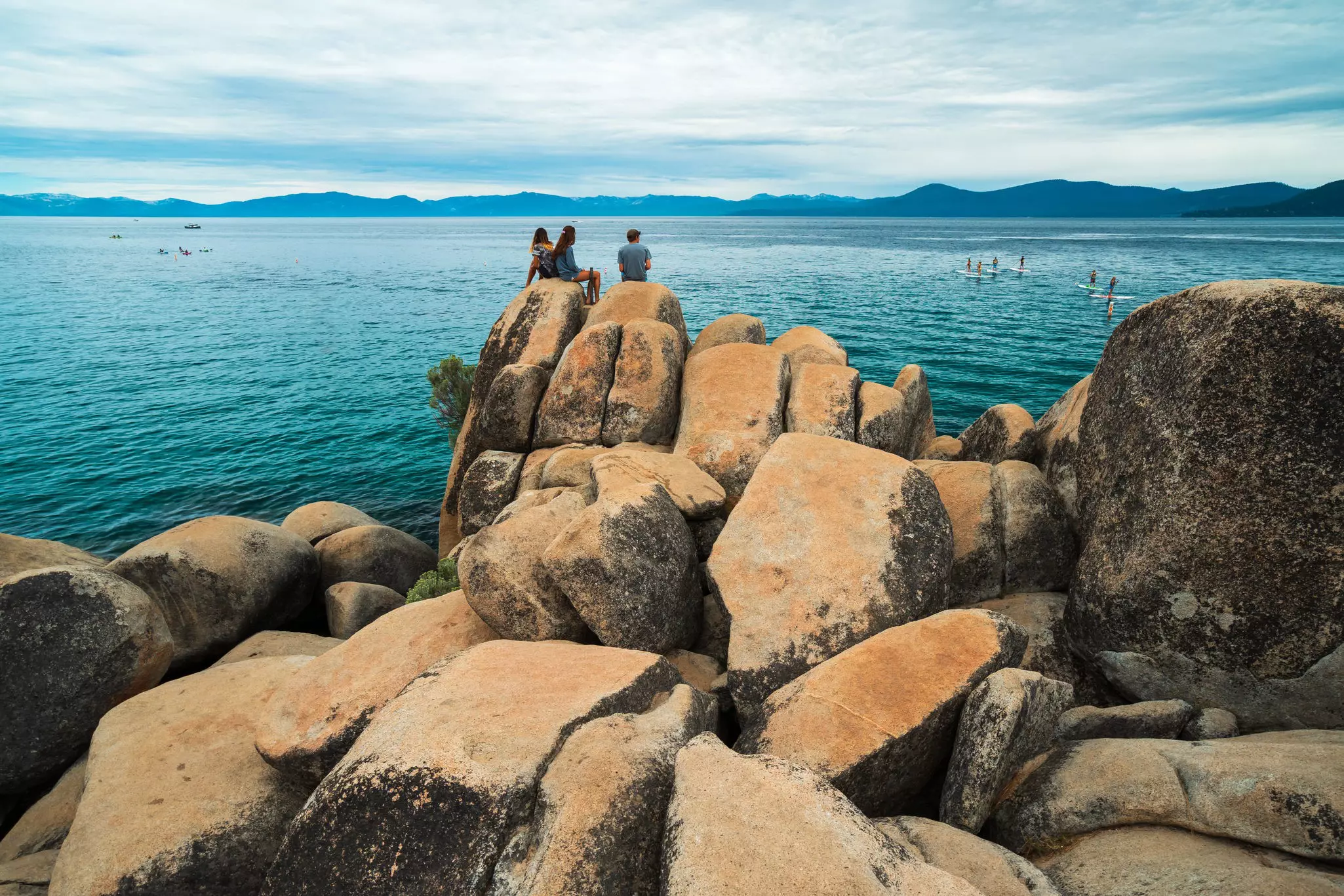 Three silhouettes sit on a large boulder overlooking a lake