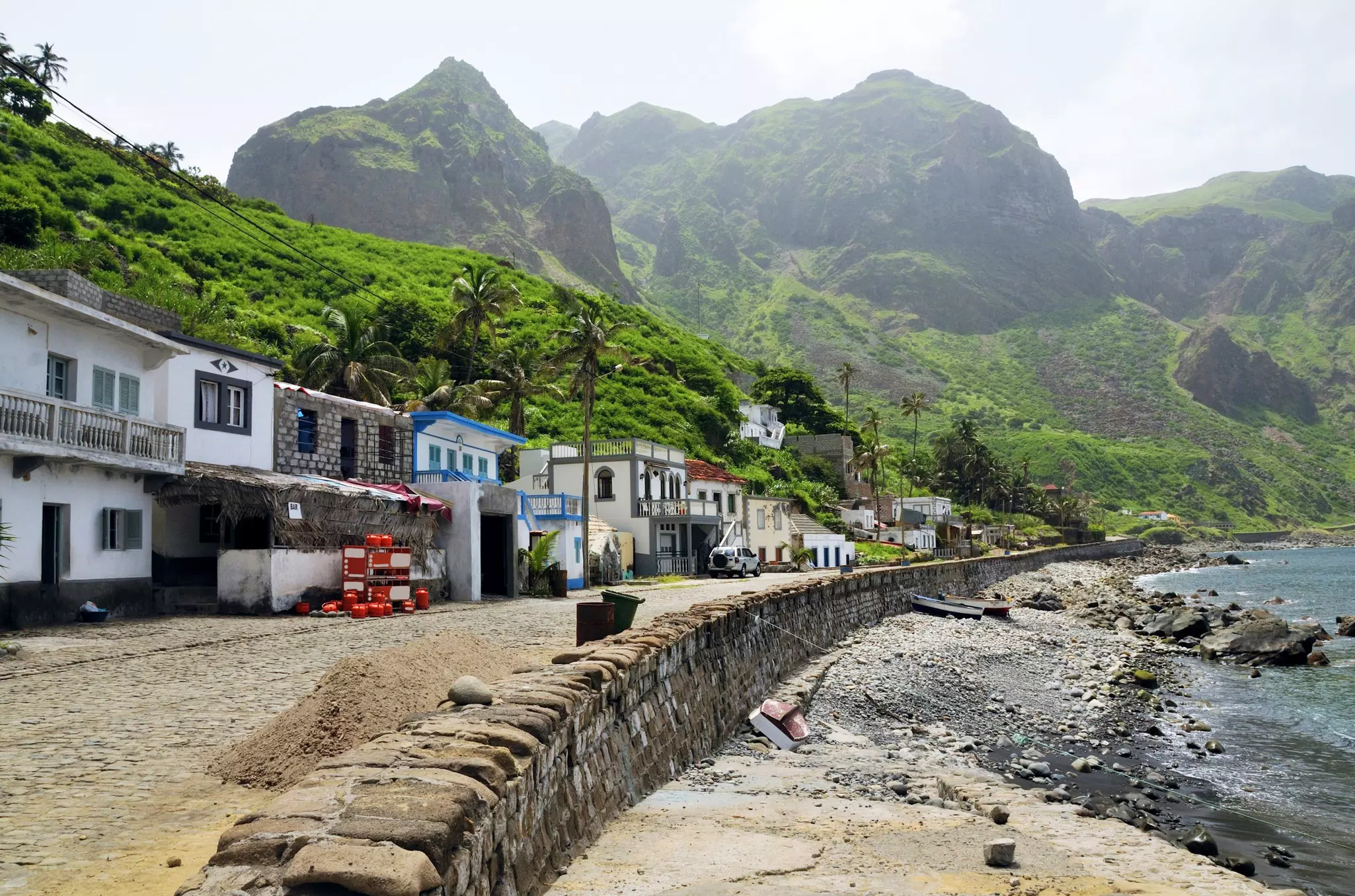 Homes and business line the oceanfront cobblestone street with lush mountains rising behind