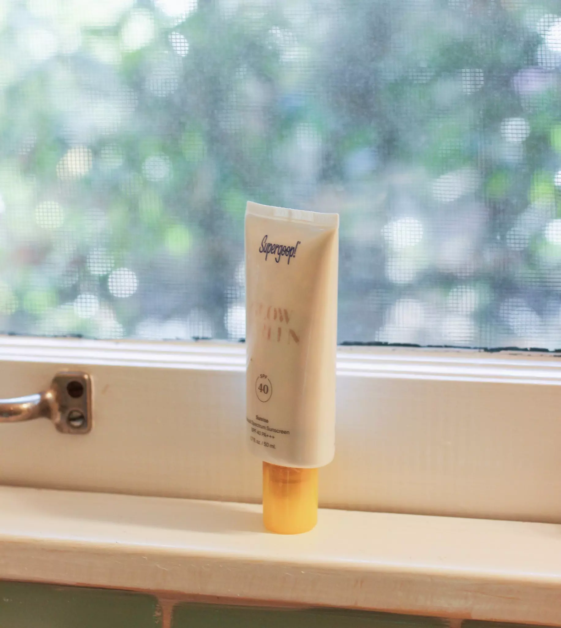 A tube of sunscreen is presented on a windowsill in a bathroom.