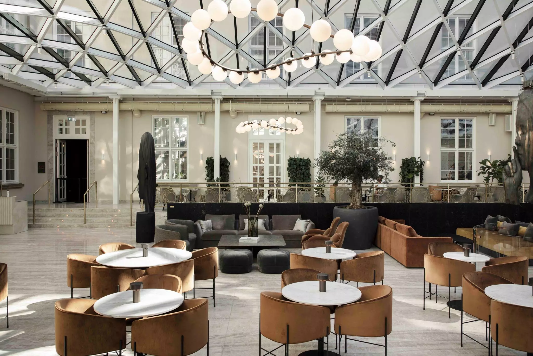 Sleek, modern furniture of brown, gray and black chairs and small round white tables arranged in a glass-roofed room