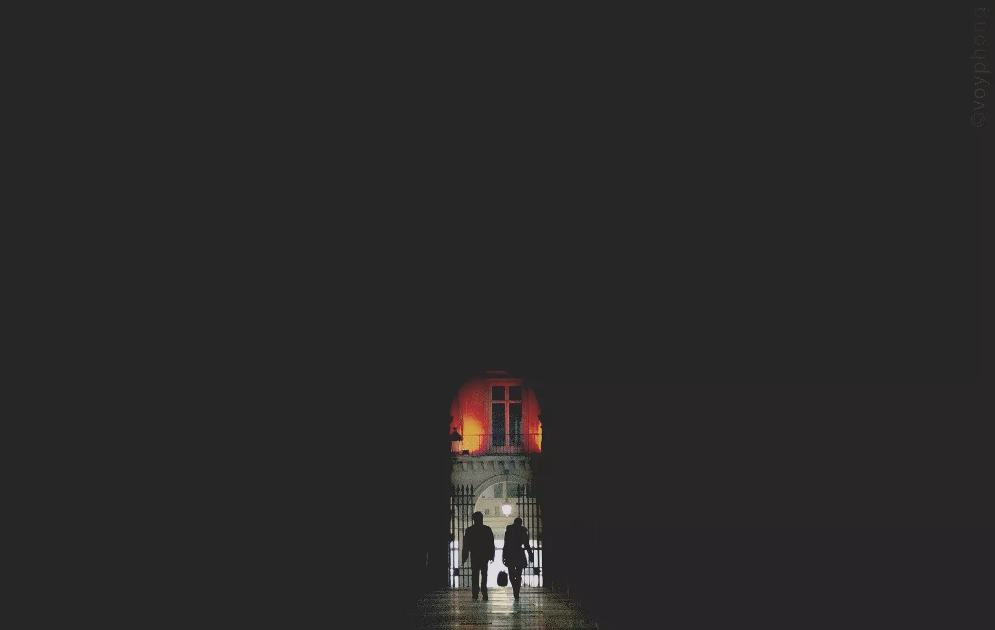 A silhouetted couple walk out of a dark passageway in Paris France and into the night, which is lit up