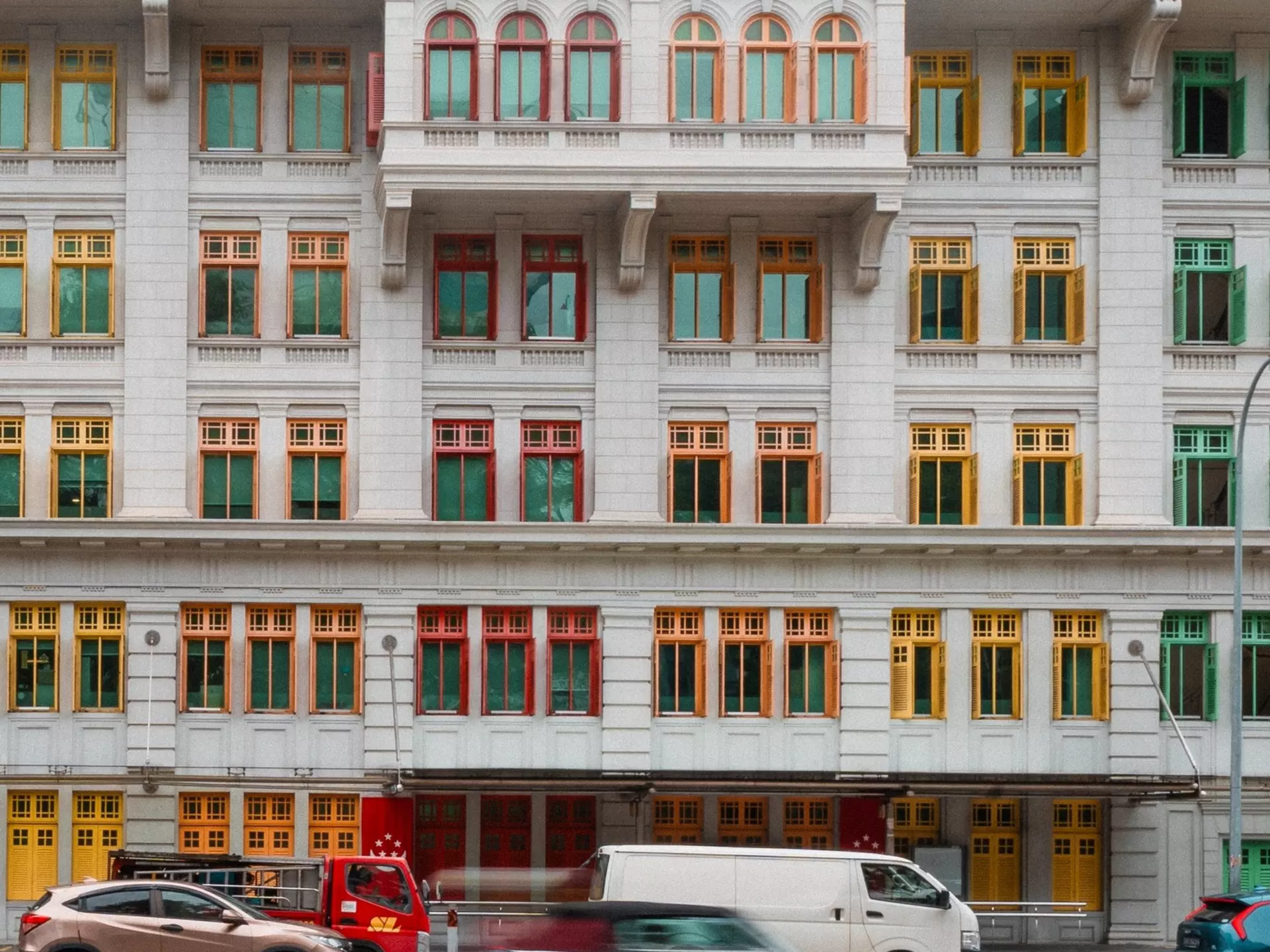 Cars speed by white buildings with colorful trim.