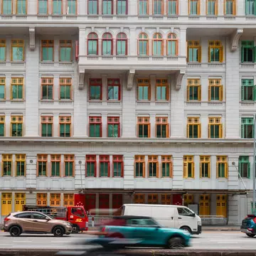 Cars speed by white buildings with colorful trim.