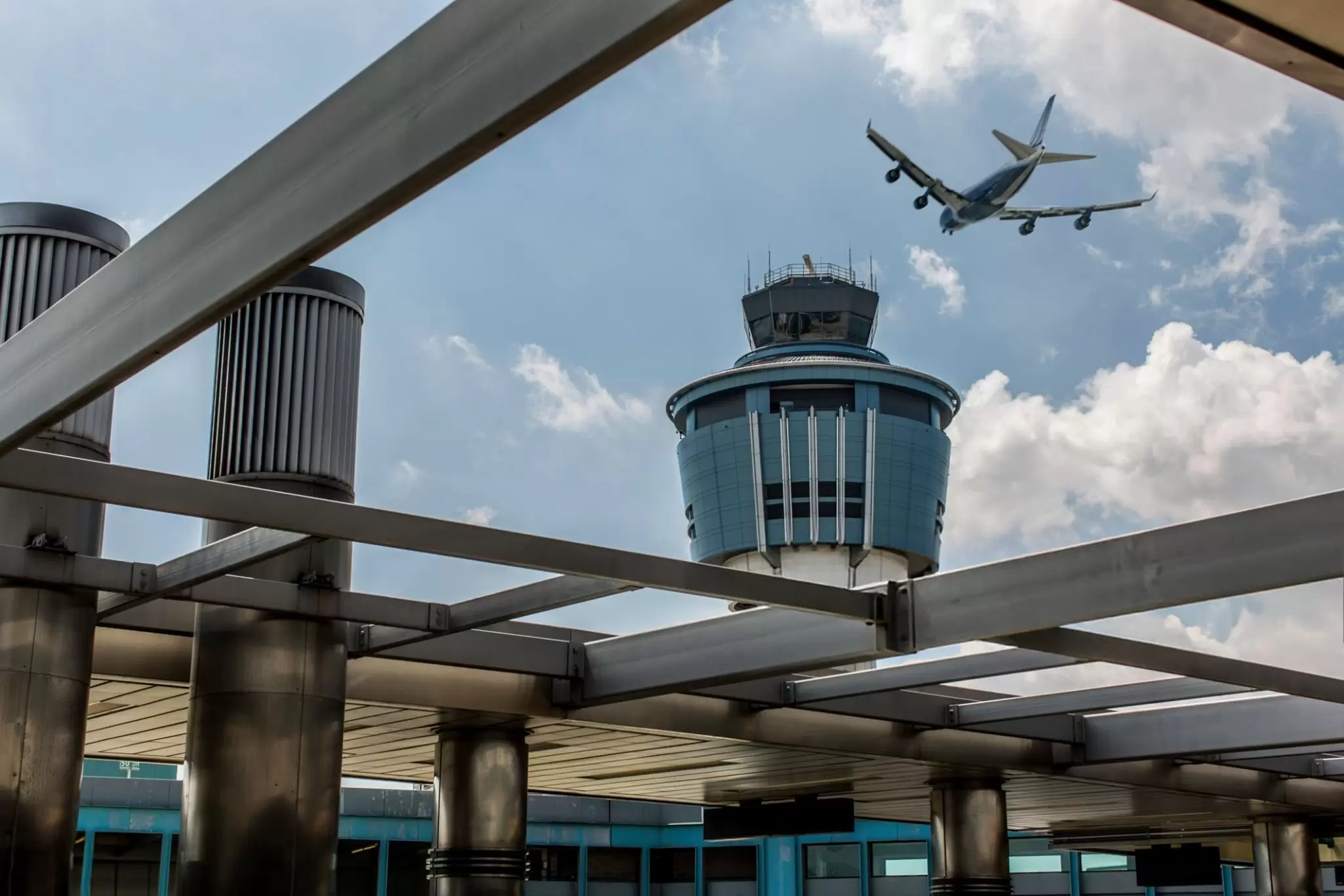A plane takes off over an air traffic control tower at LaGuardia Airport in New York City. View from the ground looking up through a metal trellis structure