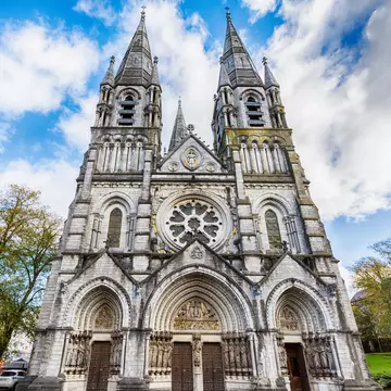 Central facade of St. Fin Barre's Cathedral in Cork, Ireland. Low angle with blue cloudy sky in the back.