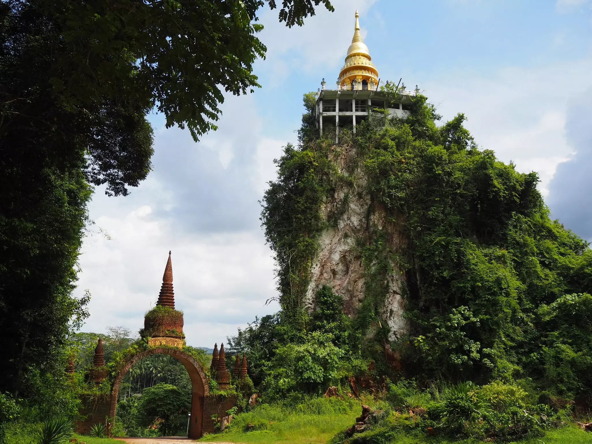 A gold-domed temple atop a grassy hill. An archway is near the foot of the hill.