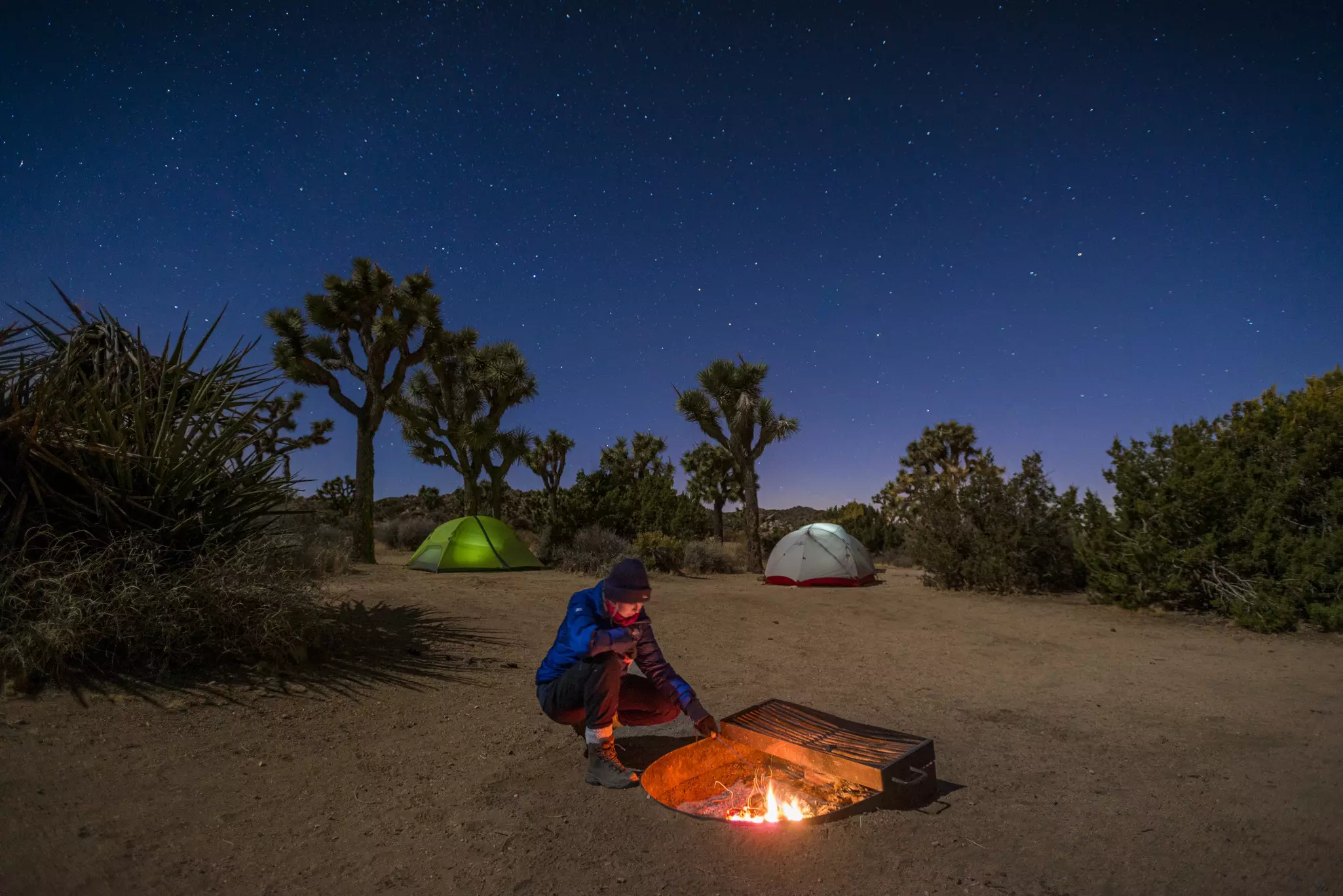 A woman stokes a camp fire near her tent at night in a national park