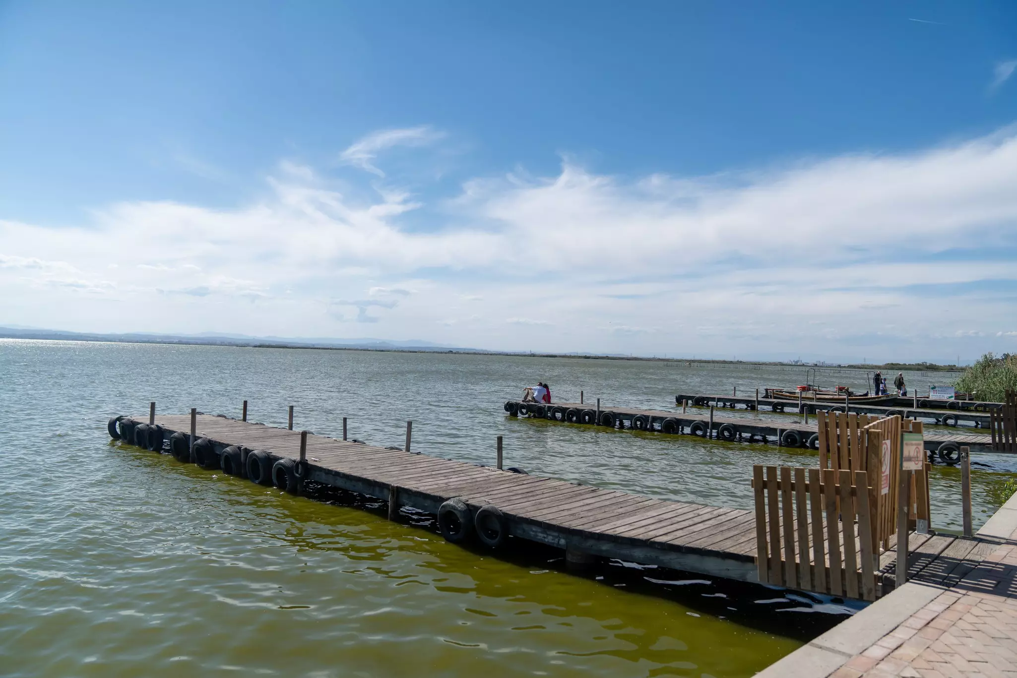 Two people sit on wooden piers that jut out into a peaceful lagoon