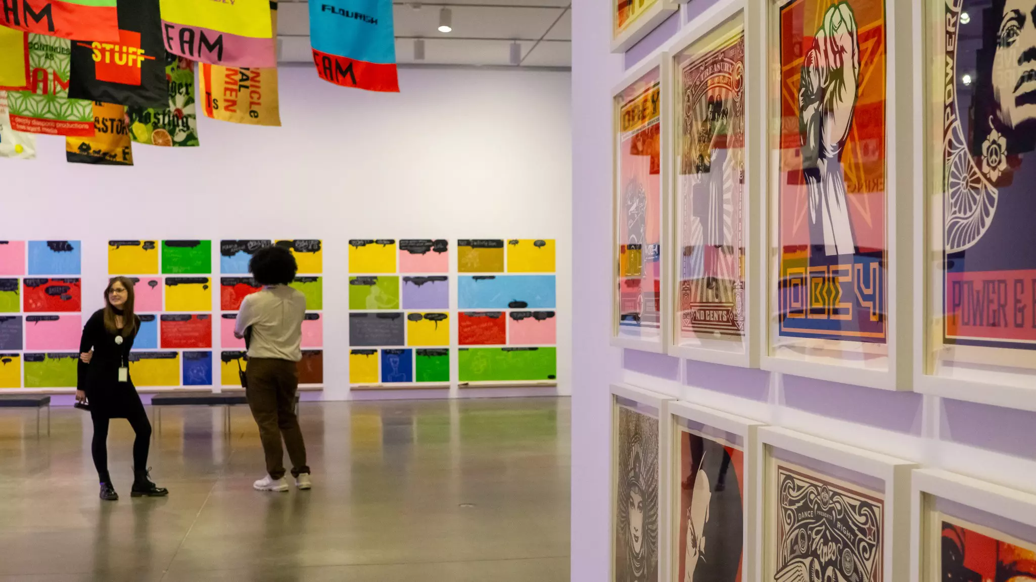 Two people stand in an art gallery lined with prints in bright colors