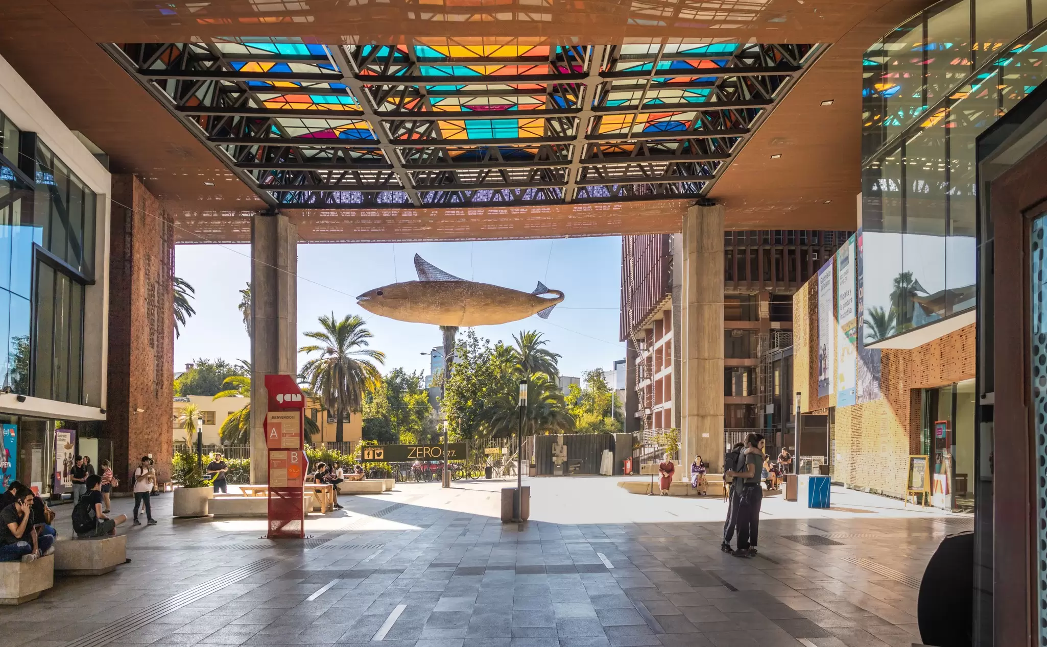 Covered plaza at Centro Gabriela Mistral, Santiago, under a stained-glass canopy, with a fish sculpture hung outside