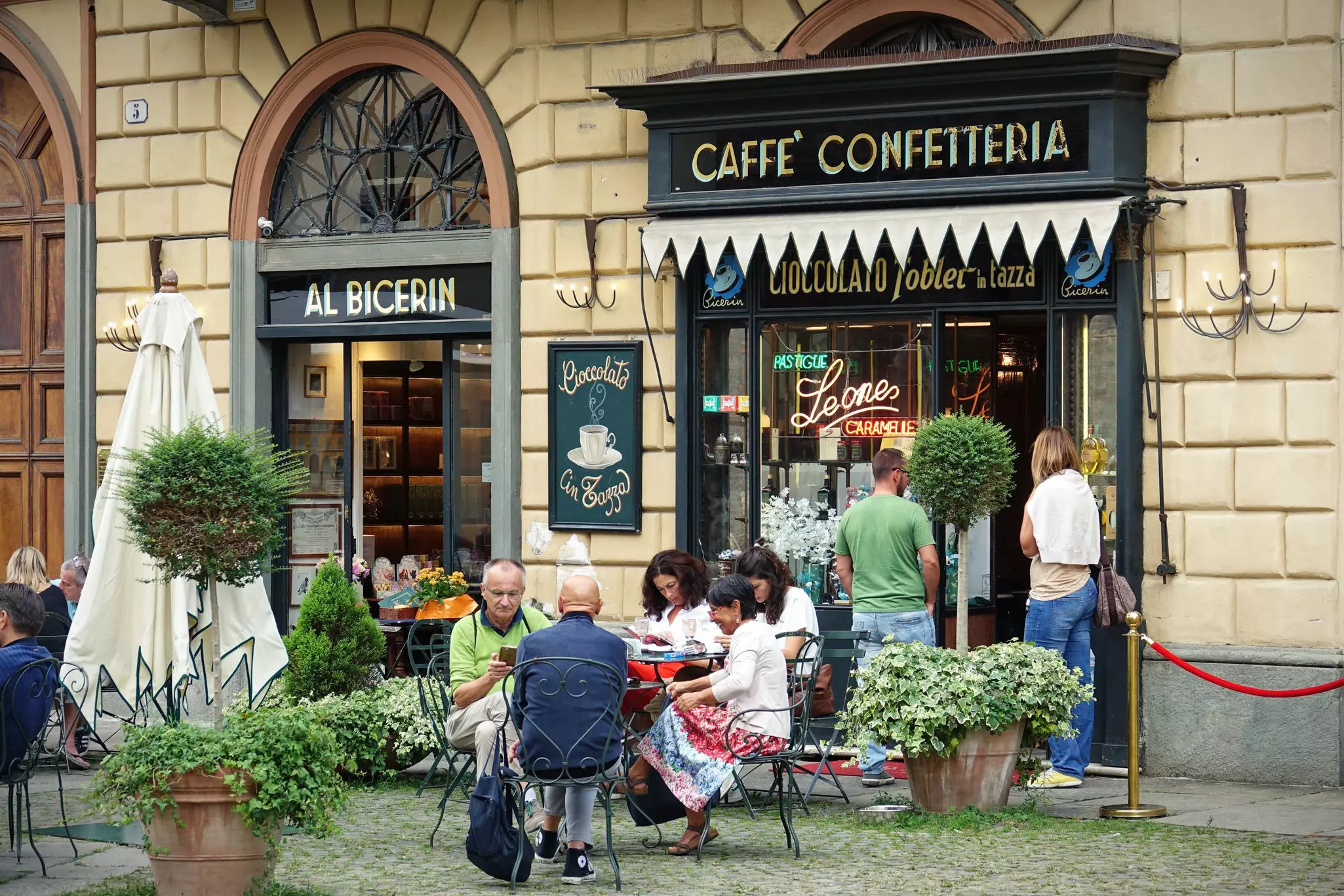 People sit at a table in front of a cafe in a city.