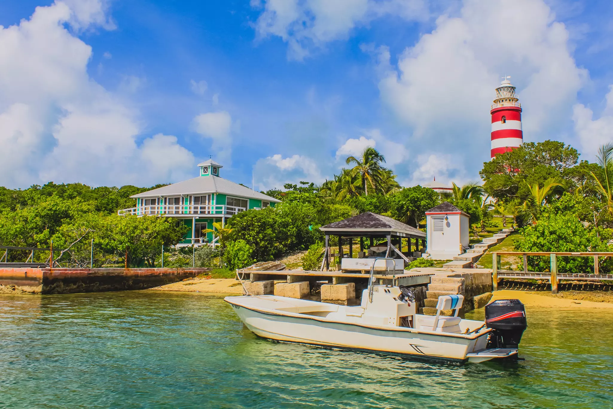 A red and white lighthouse stands tall above tropical vegetation on the shoreline.