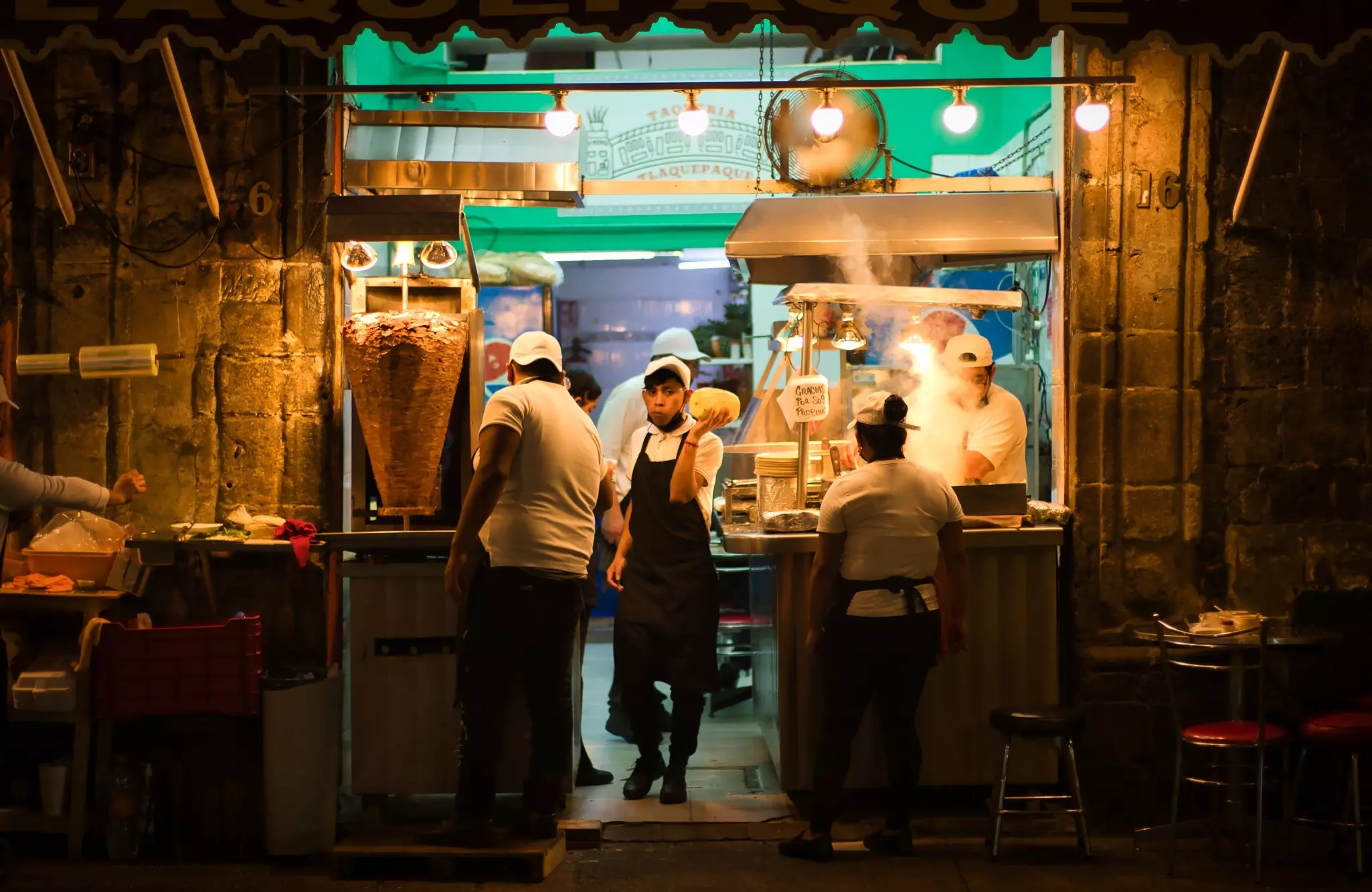 Chefs in aprons cook tacos and other food at a stall in a city street at night.