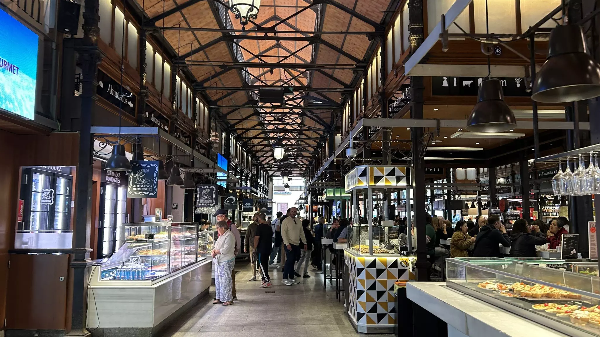 People in an aisle of a large indoor market with high ceilings and beams