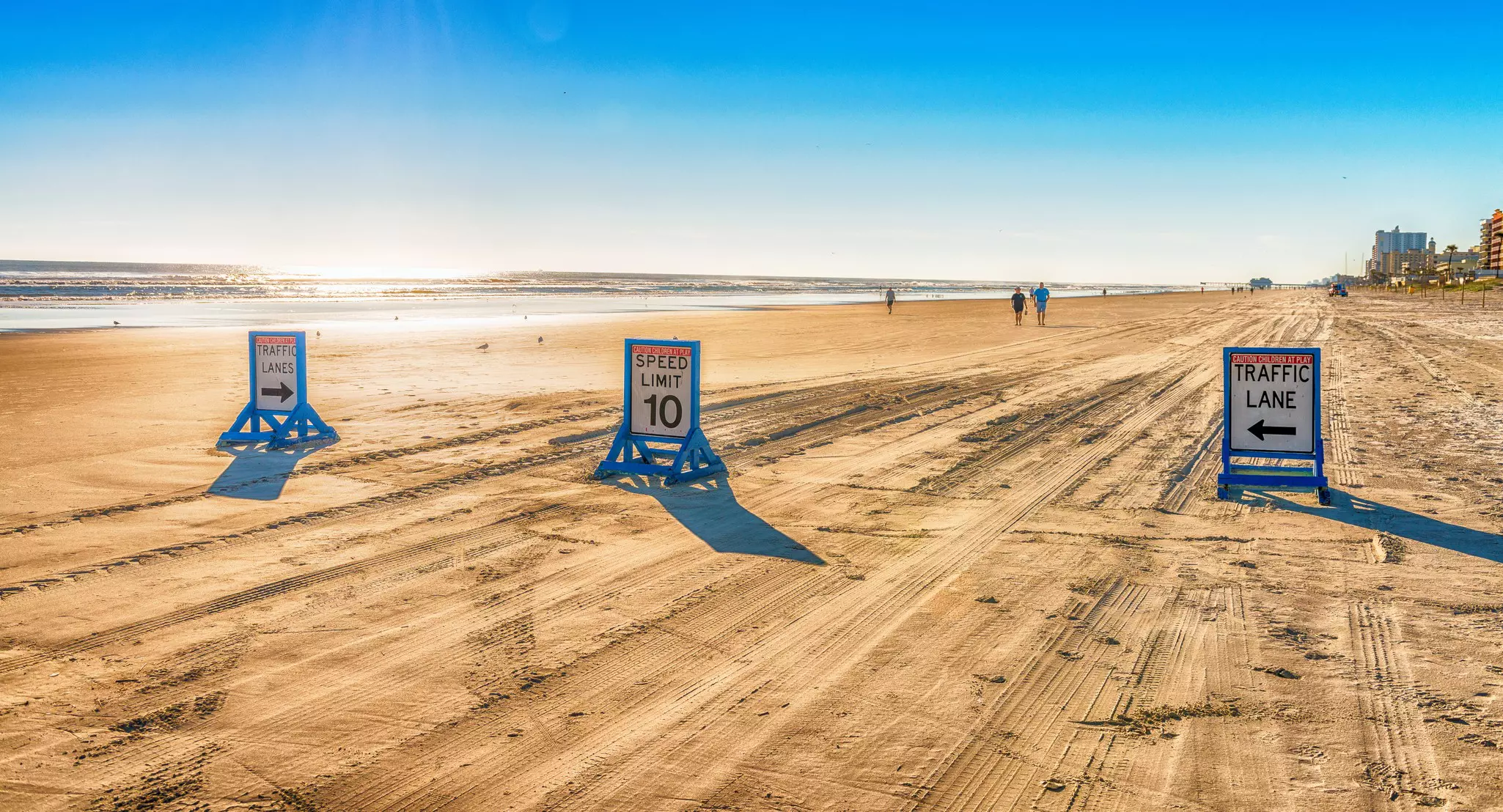 Three signs direct traffic on a beach. Tire tracks are visible on the sand.