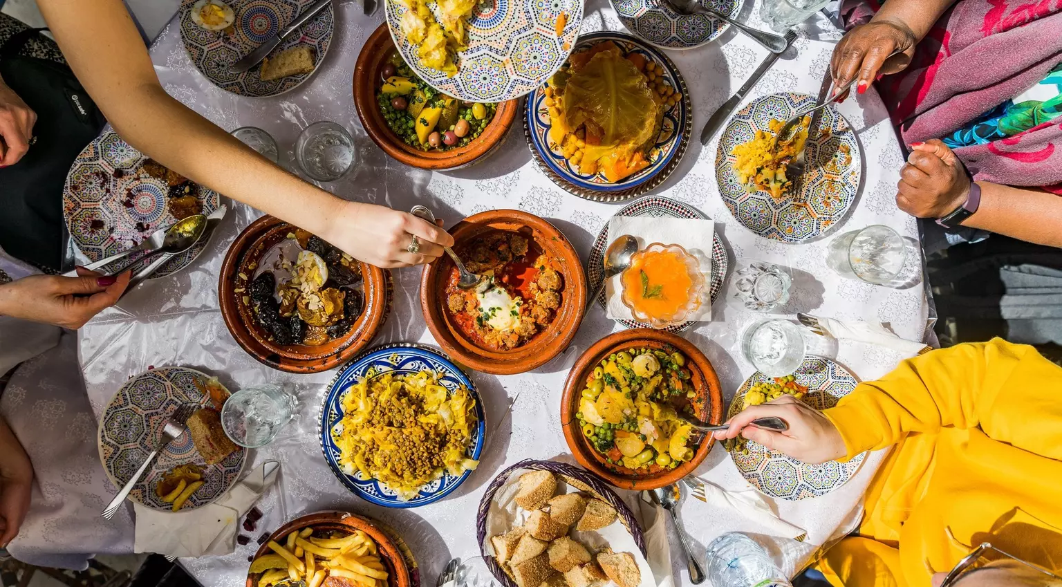 Top view of a colorful Moroccan meal with traditional tagines and dishes shared among friends, showcasing vibrant cuisine and cultural dining in Morocco.
