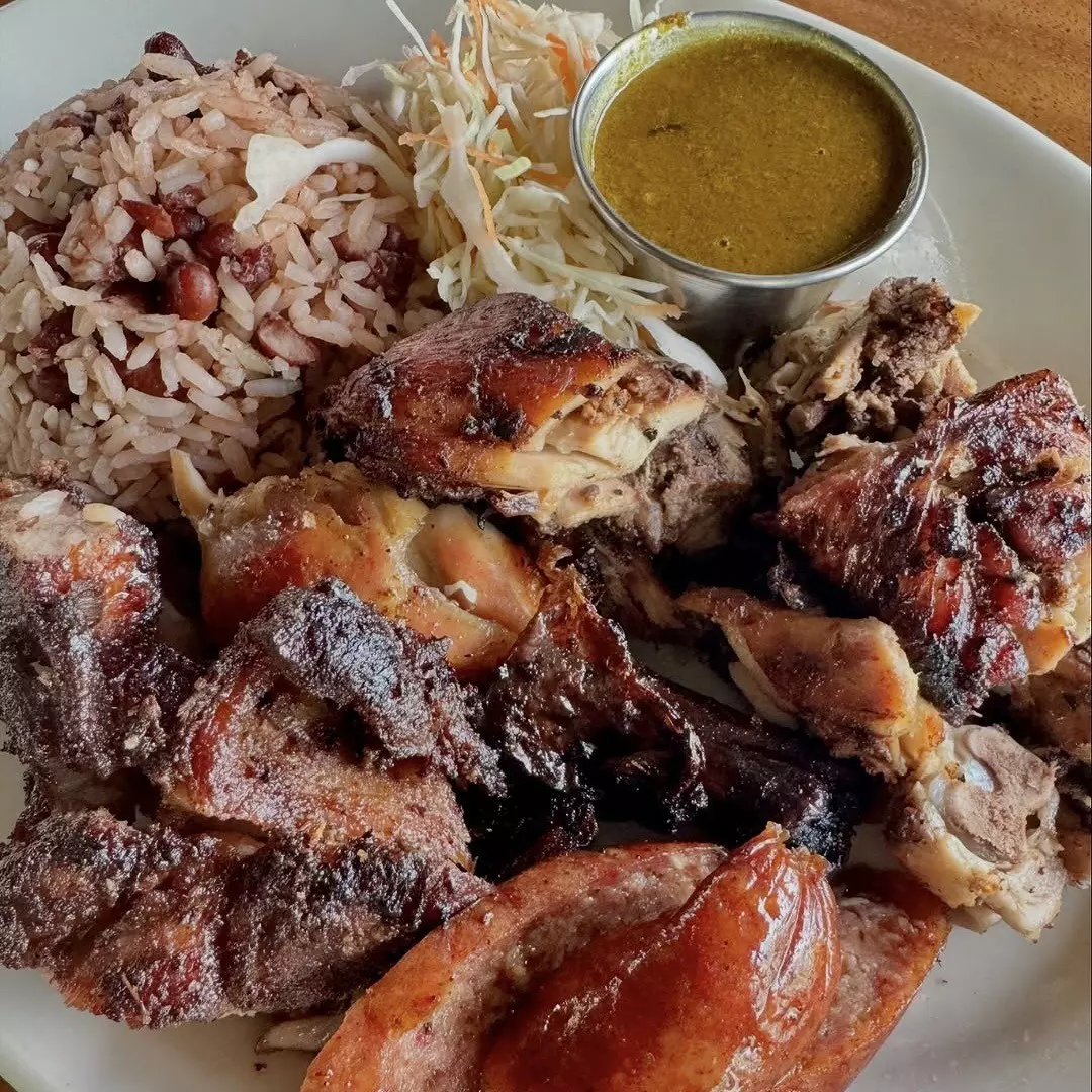 A close-up shot of a dish of jerk chicken, rice and pepper sauce