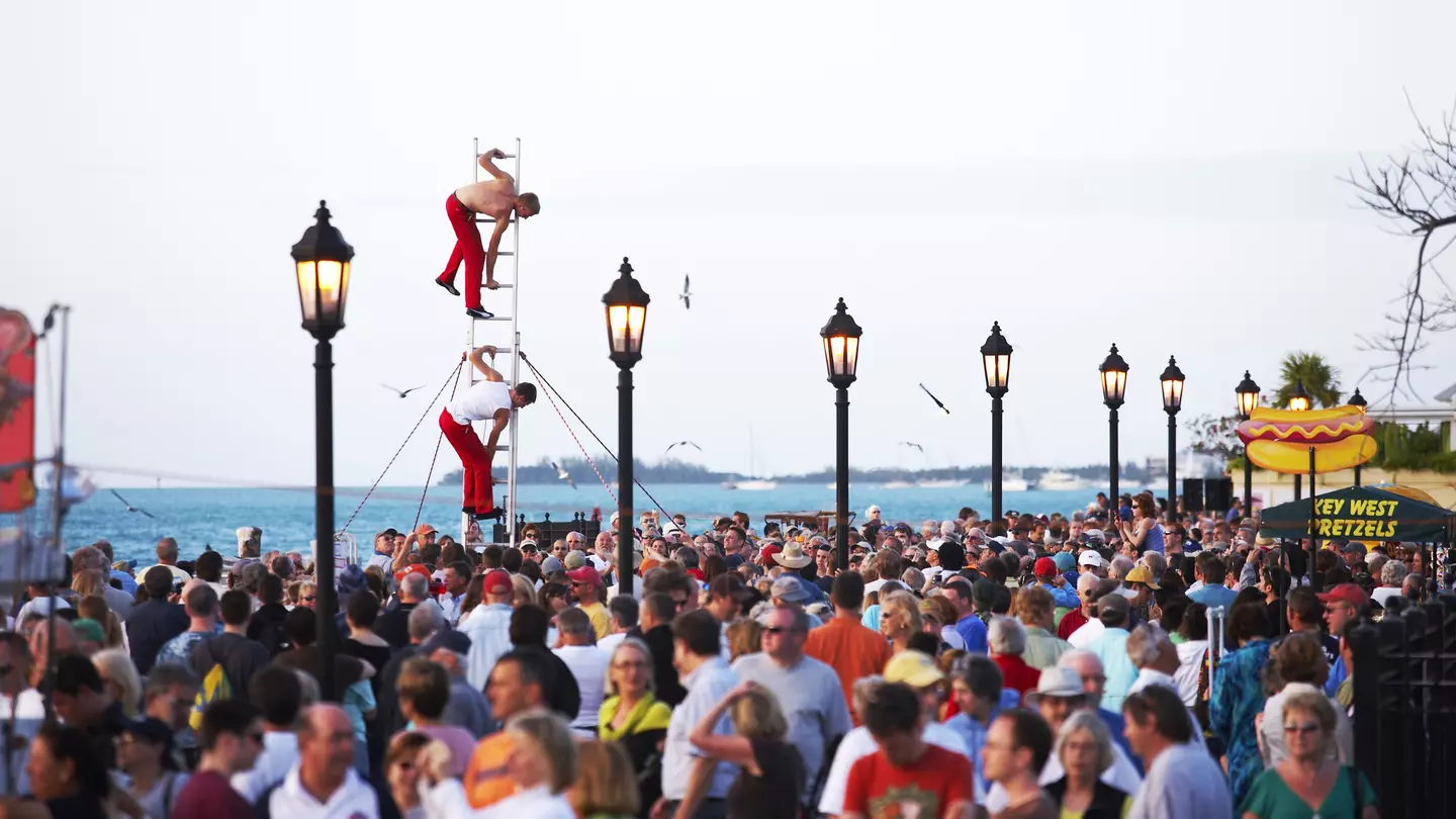 A crowd on an ocean promenade with street performers balanced on a ladder.