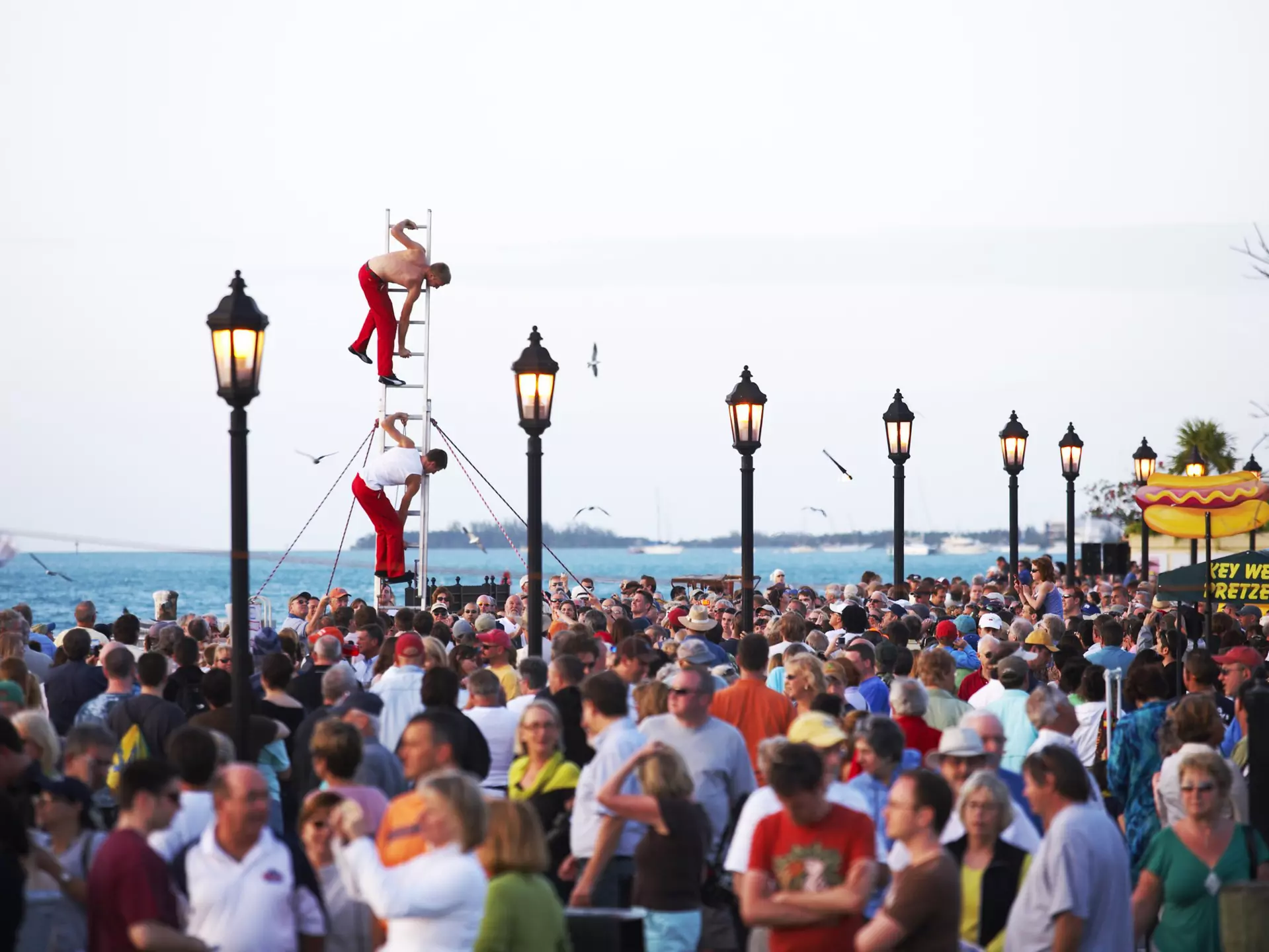 A crowd on an ocean promenade with street performers balanced on a ladder.