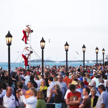 A crowd on an ocean promenade with street performers balanced on a ladder.