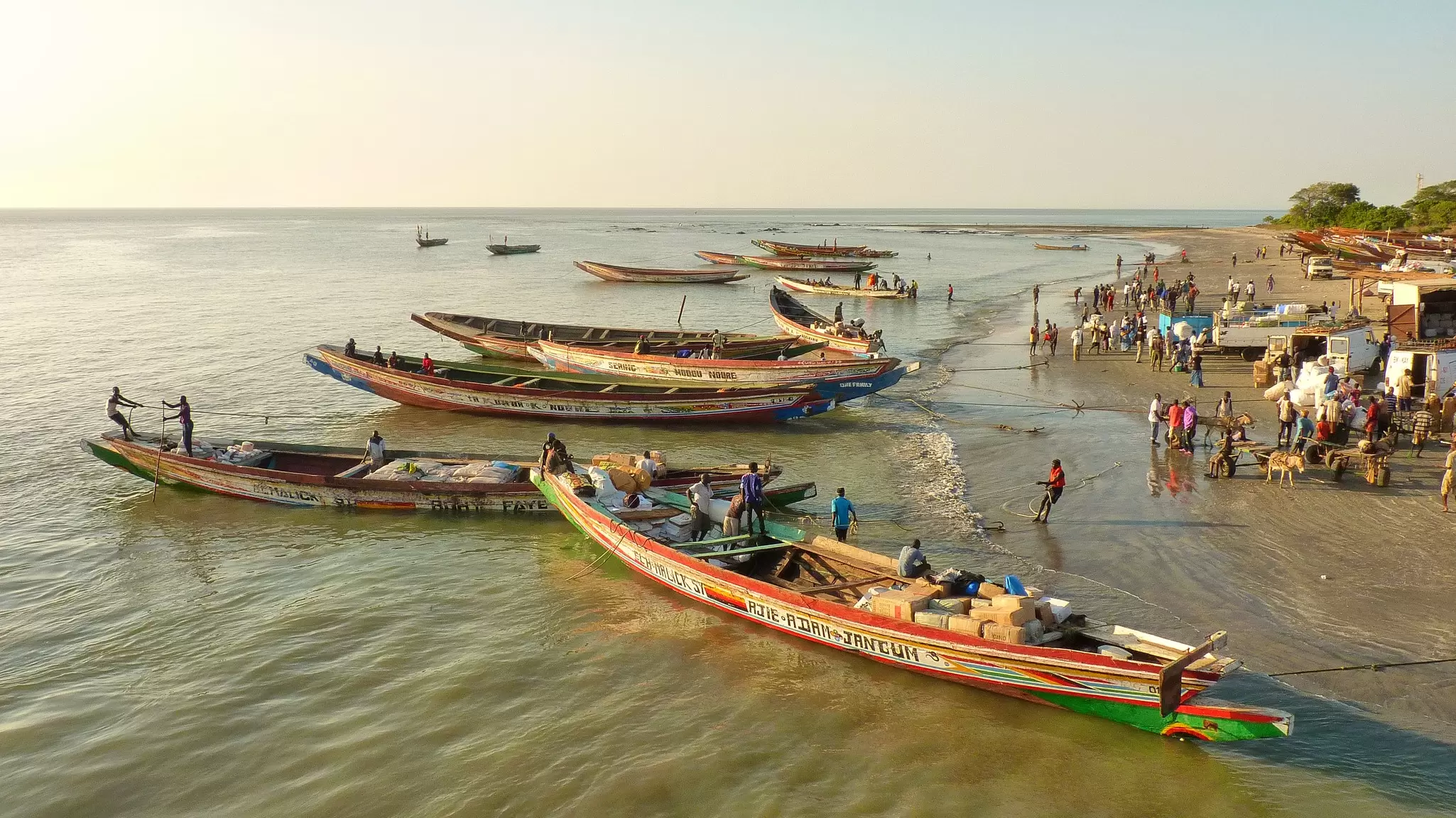 Large open boats docked on the bank of a wide river.