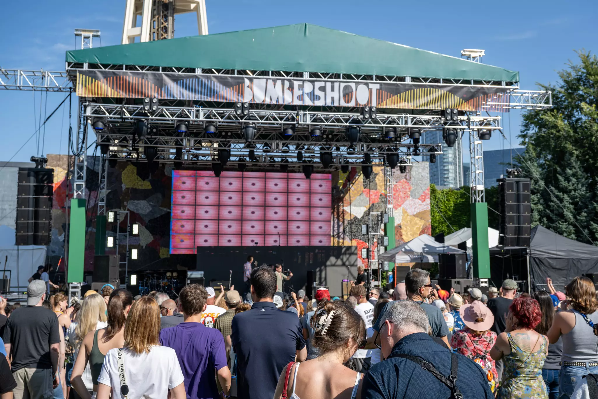 Crowds of people gather in front of a stage at a daytime music festival.