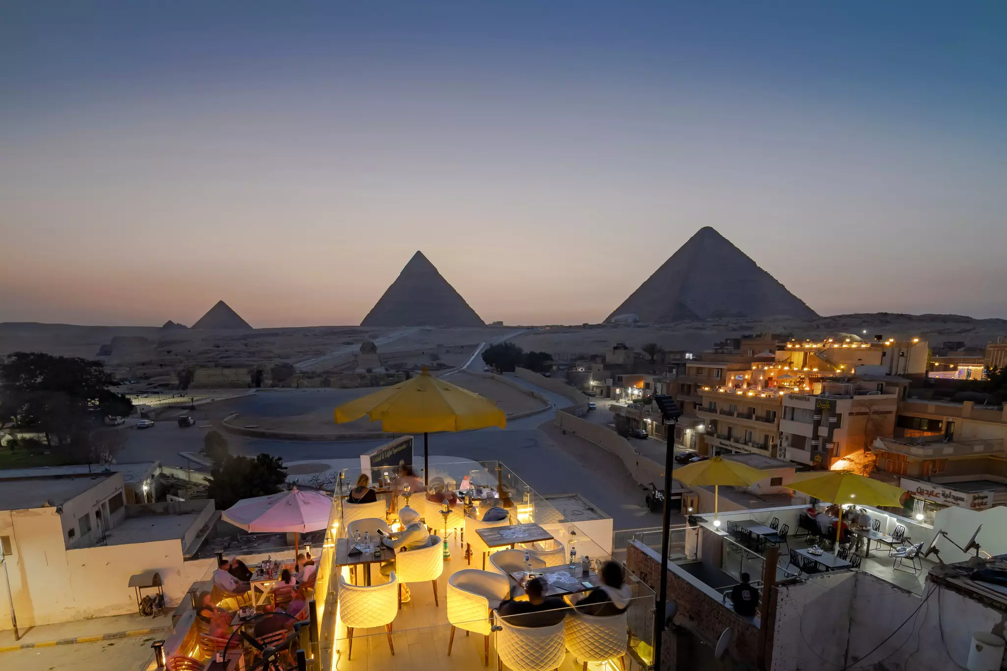 Tourists watching sunset over the Pyramids from a rooftop lounge, Giza, Egypt.