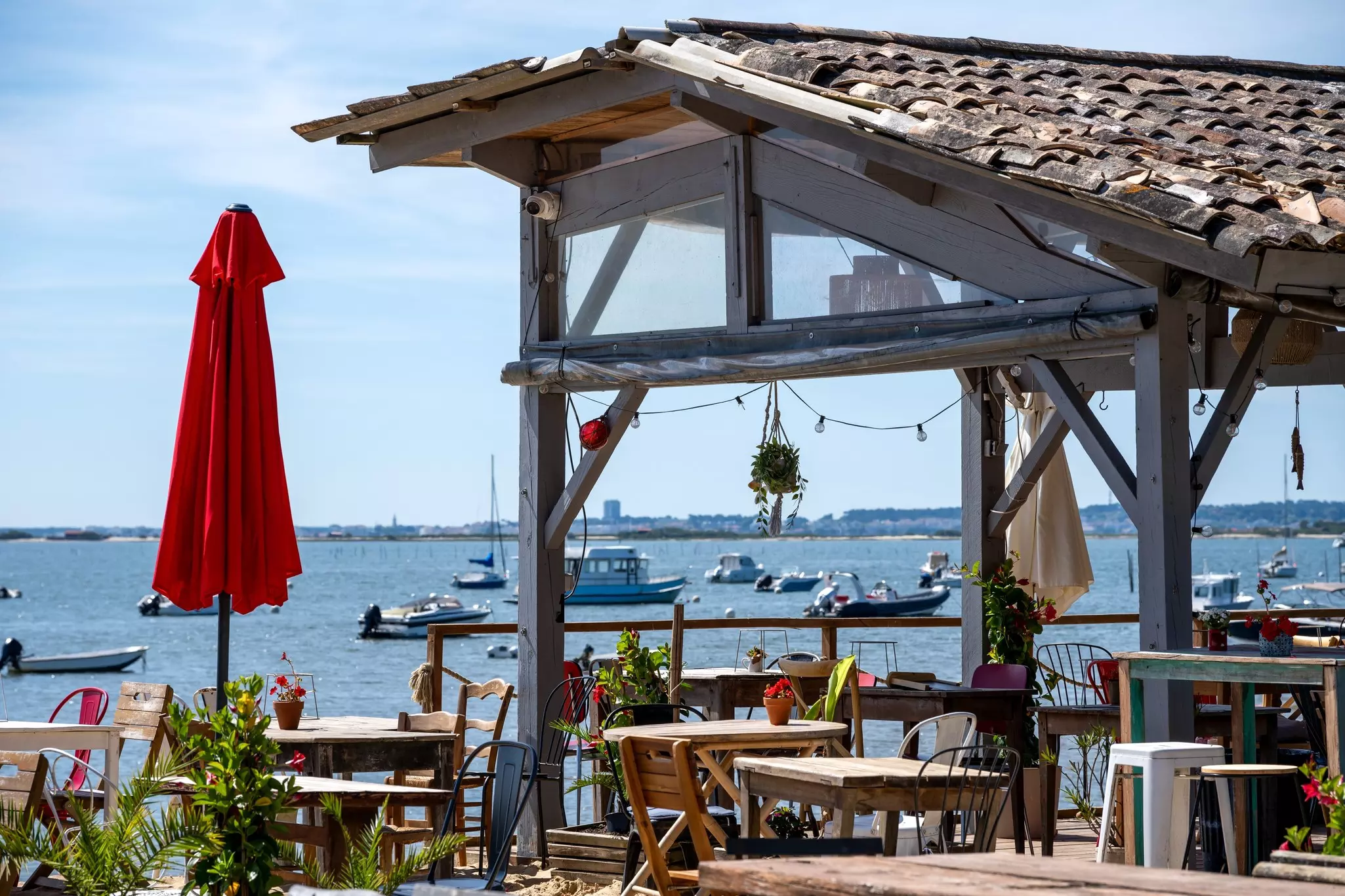 A cafe by the water has outdoor tables and a closed red umbrella.