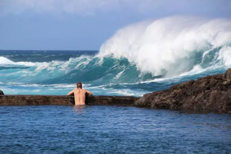 A man watches waves break from a natural rock pool in Madeira, Portugal. 