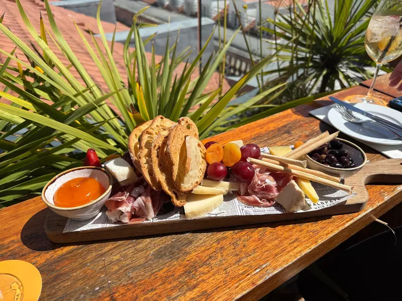 A platter of meat, cheese, fruit, breads and spreads on a wood plank in the sunshine.