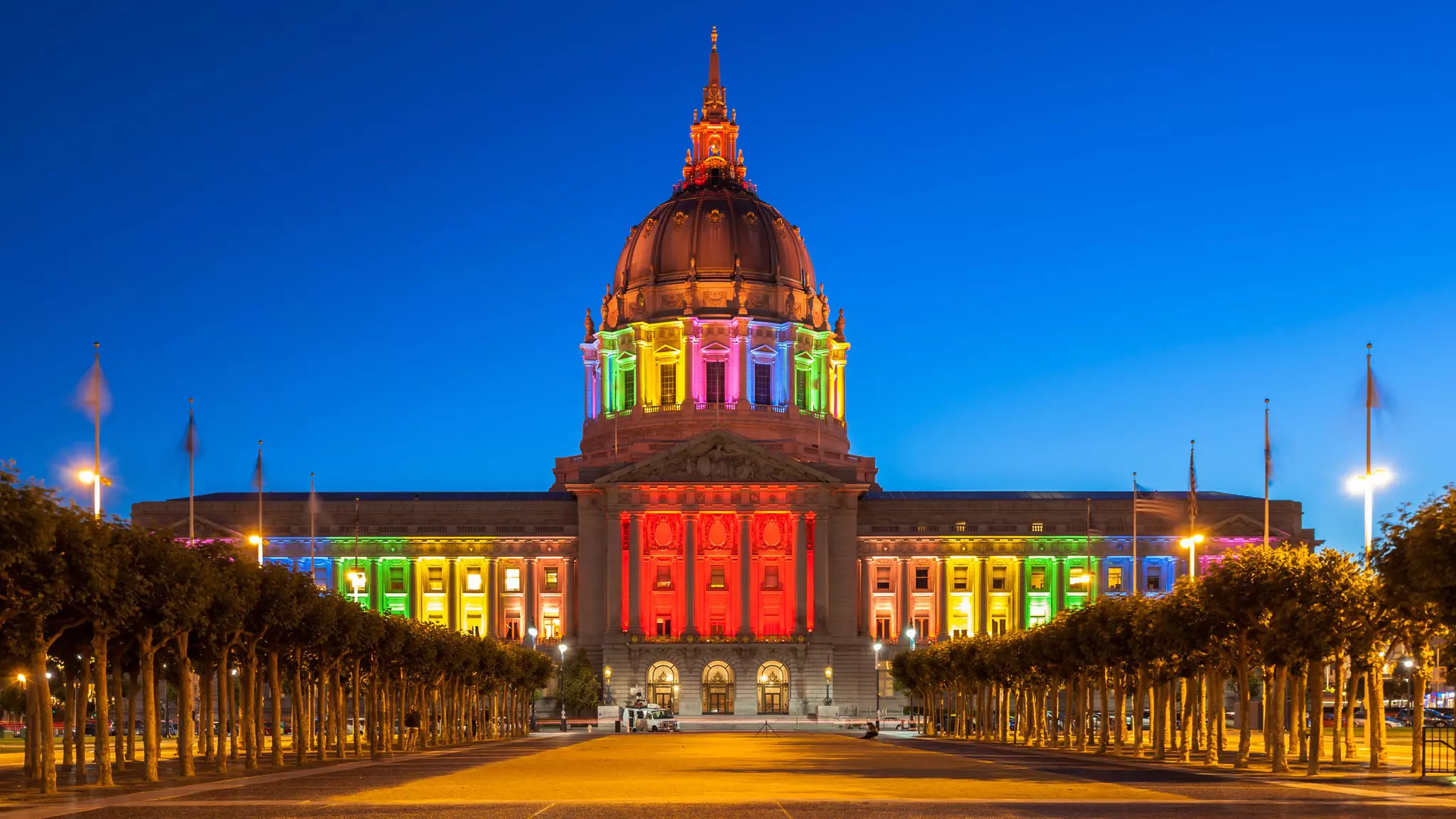 Evening shot of San Francisco City Hall illuminated in rainbow-colored lights.