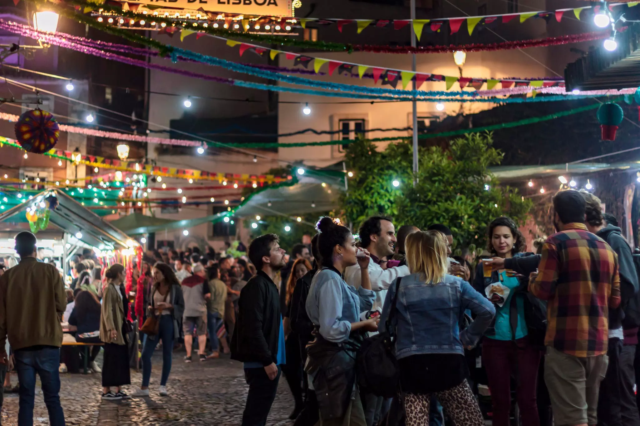 People gathered at a street party at night during a festival. Flags and decorations fly above them.