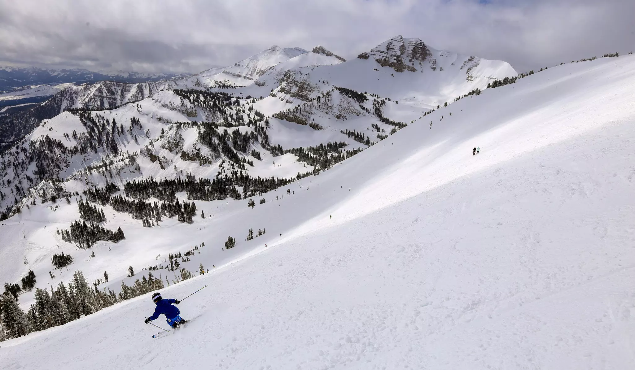 A person skiing downhill on a large, snowy mountain range