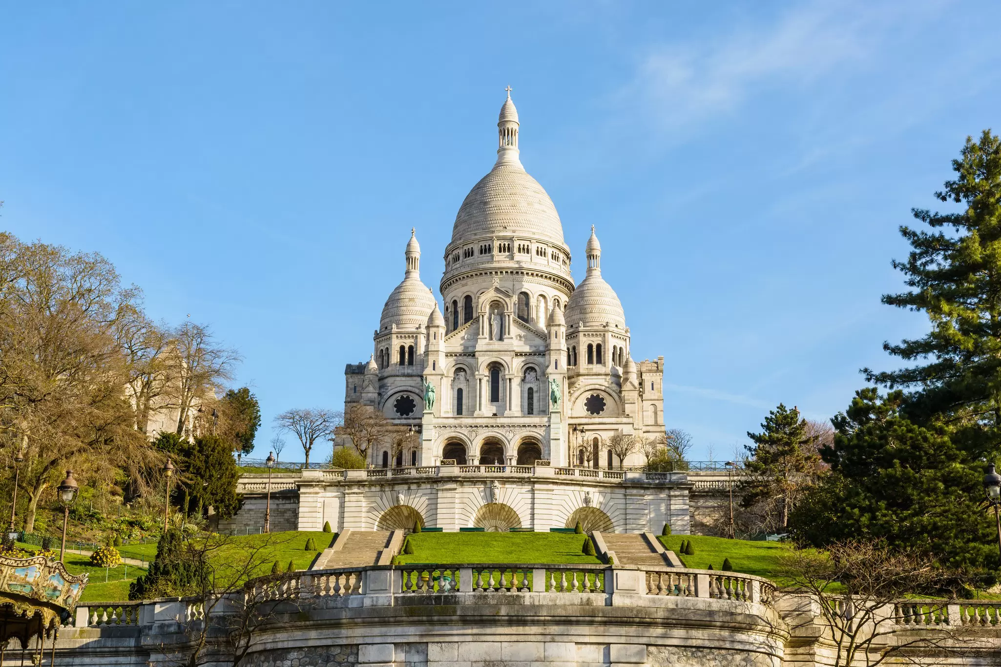 The basilica of the Sacred Heart of Paris under a blue sky in springtime seen from the bottom of the Louise Michel park, with the terrace and stairways on the foreground.