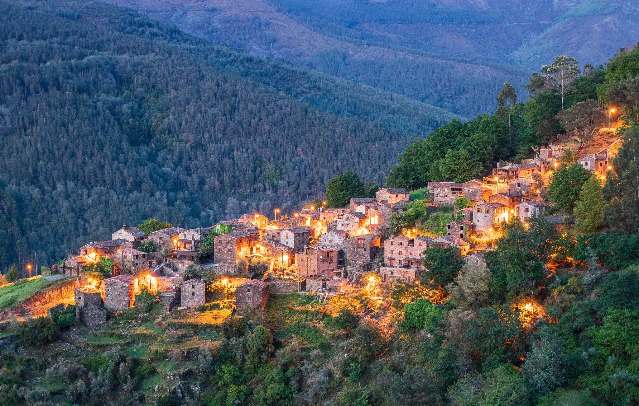 A series of stone cottages tucked into the folds of a forest-covered valley
