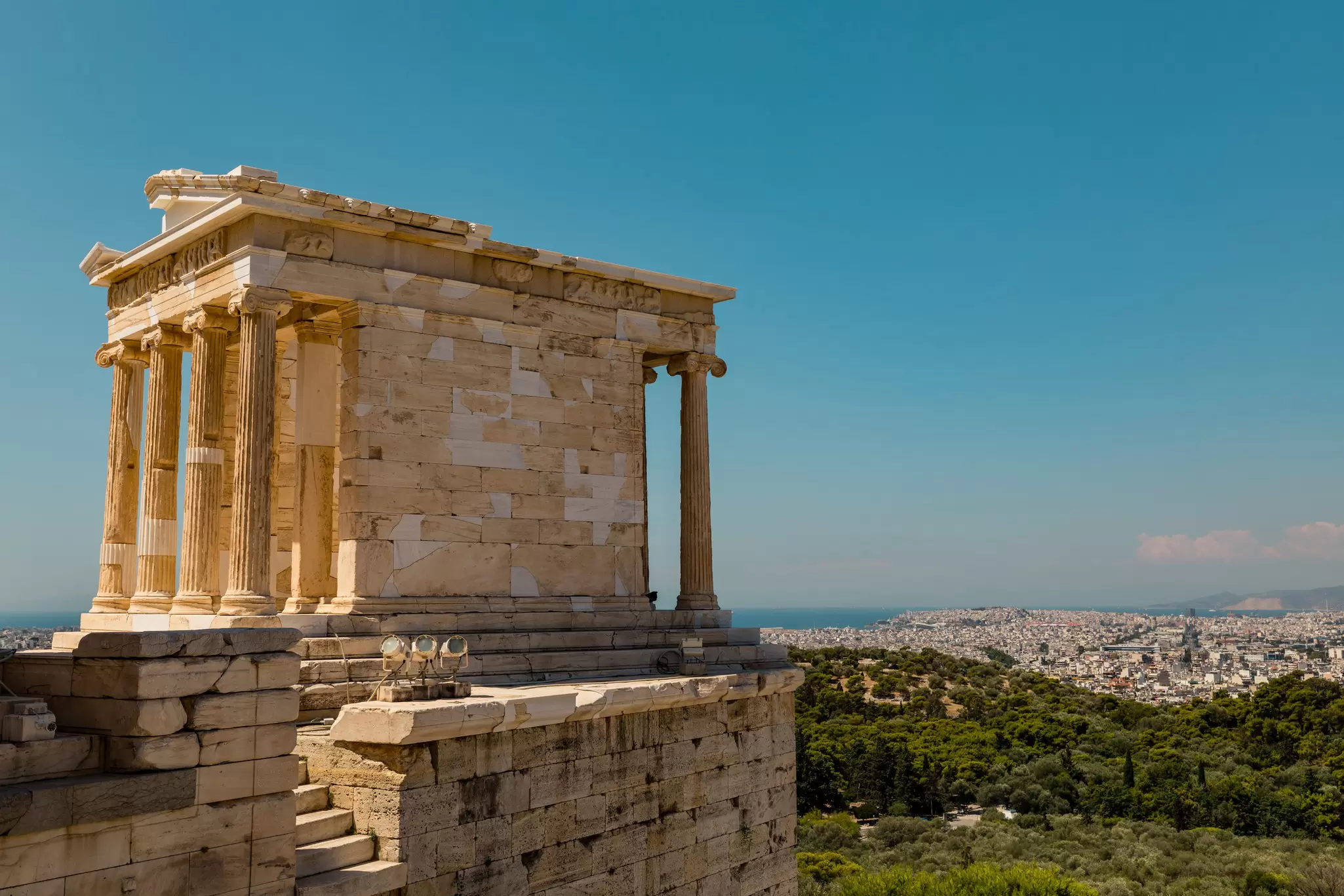 The Ancient Temple of Athena Nike on the Acropolis hill stands tall over Athens with the coastline on the horizon.